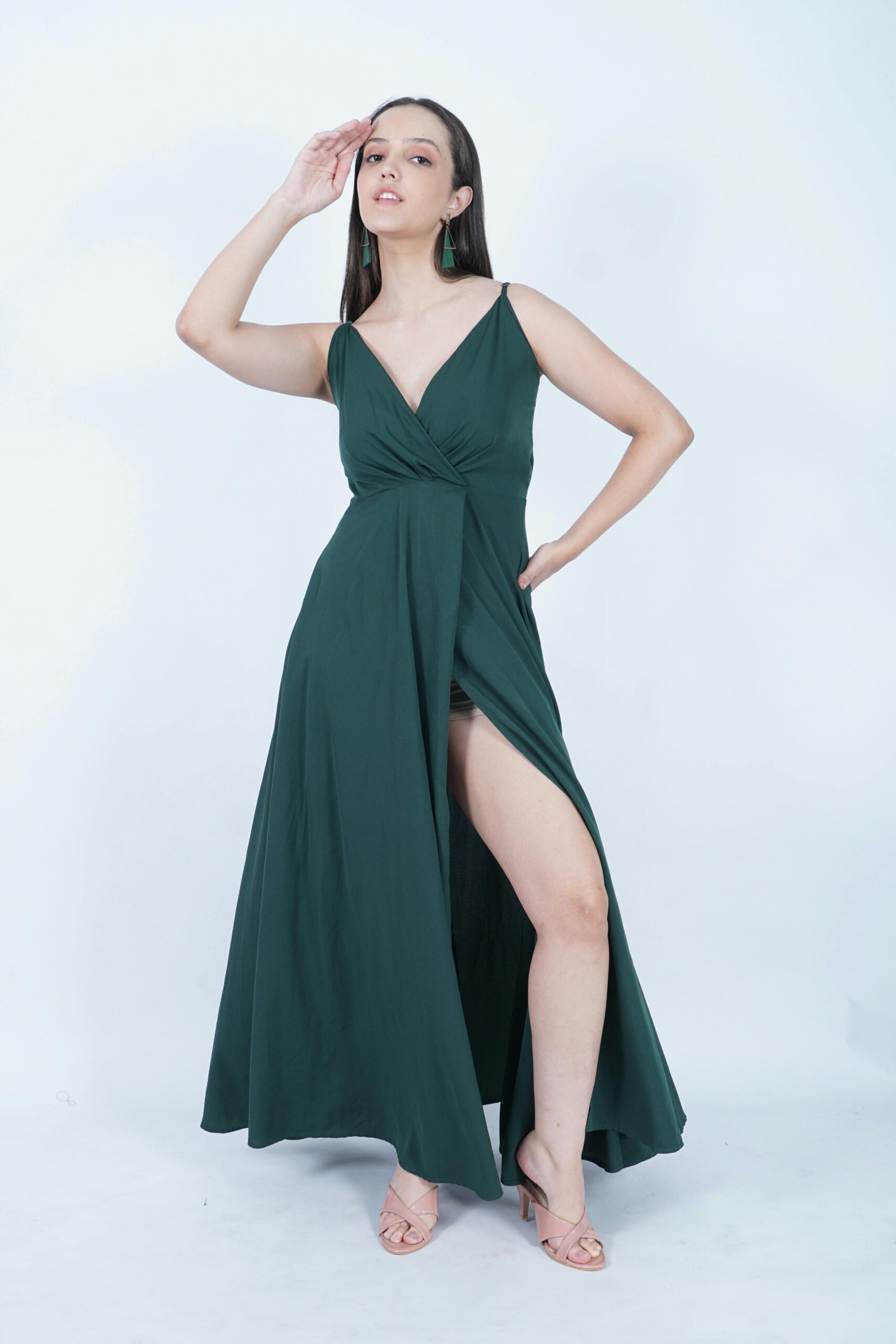Fashionable woman in a long green dress posing elegantly in a studio setting.
