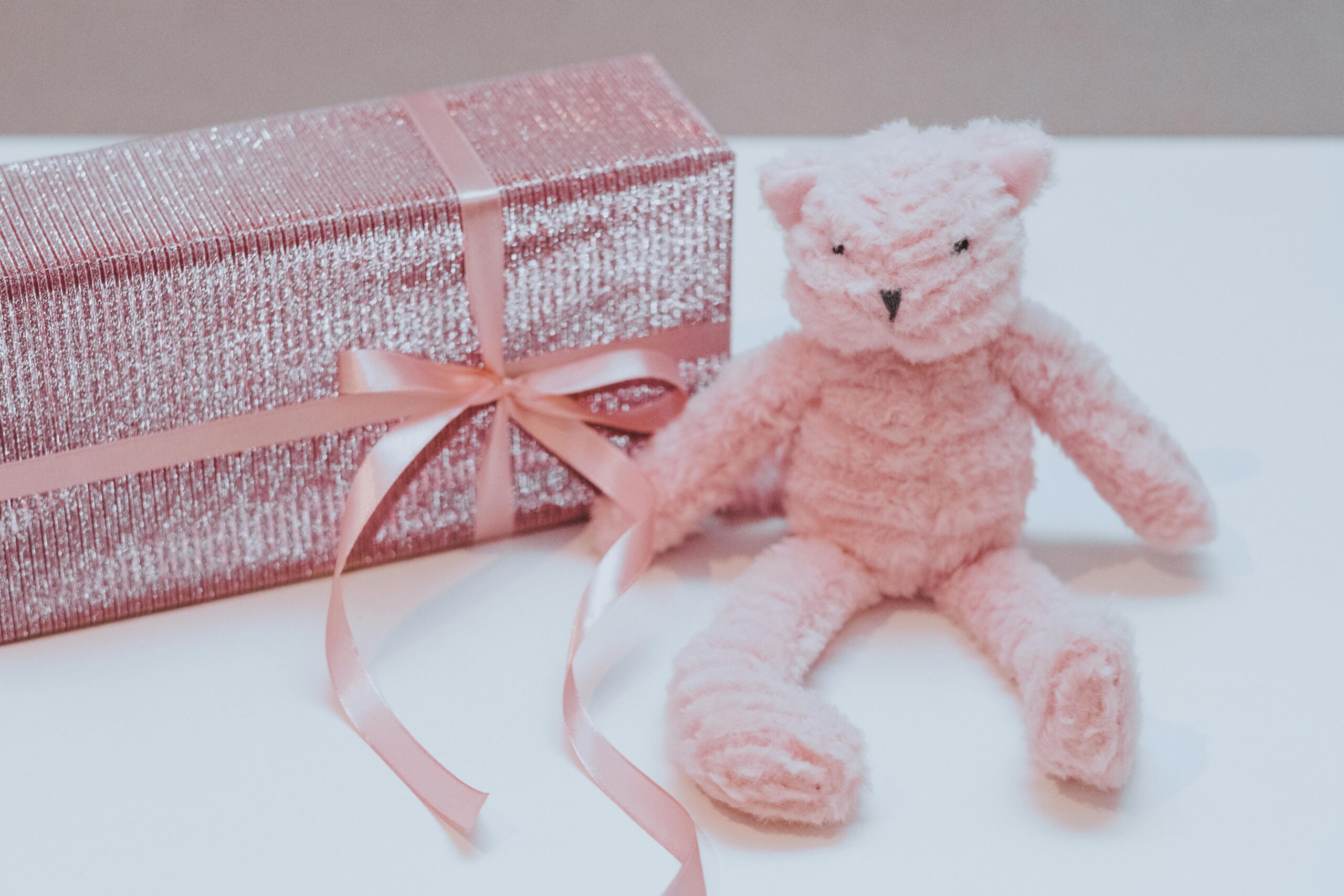 Charming still life of a pink plush toy and gift box, wrapped with pink ribbon.